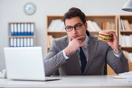 Hungry funny businessman eating junk food sandwichの写真素材