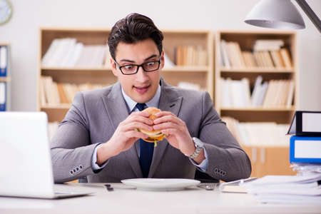 Hungry funny businessman eating junk food sandwichの写真素材