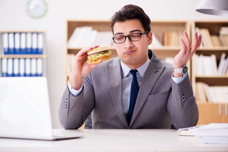 Hungry funny businessman eating junk food sandwichの写真素材