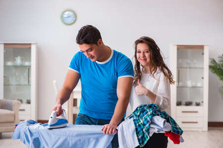 Man husband ironing at home helping his wifeの写真素材