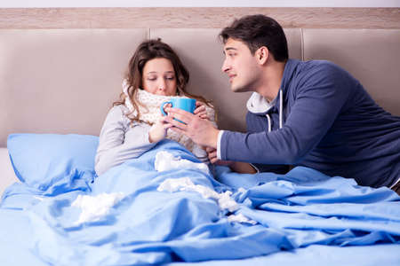 Wife caring for sick husband at home in bedの写真素材