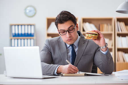 Hungry funny businessman eating junk food sandwichの写真素材