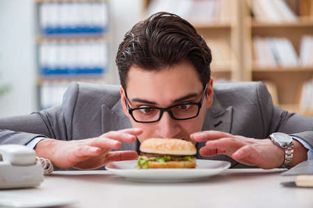 Hungry funny businessman eating junk food sandwichの写真素材