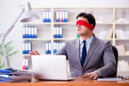 Blindfold businessman sitting at desk in officeの写真素材