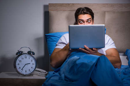 Young man working on laptop in bedの写真素材