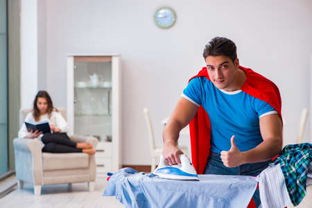Super hero man husband ironing at home helping his wifeの写真素材