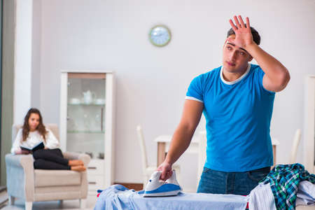 Man husband ironing at home helping his wifeの写真素材