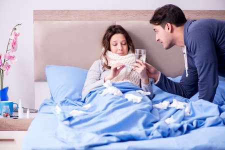 Wife caring for sick husband at home in bedの写真素材