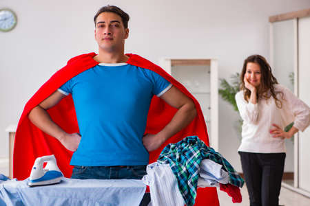 Super hero man husband ironing at home helping his wifeの写真素材