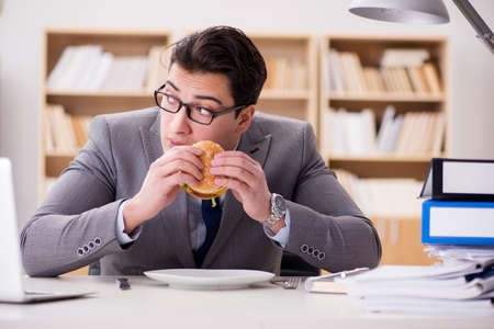 Hungry funny businessman eating junk food sandwichの写真素材