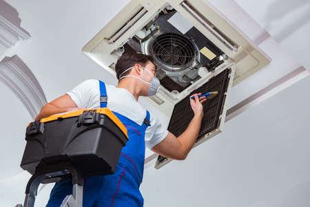 Worker repairing ceiling air conditioning unitの写真素材