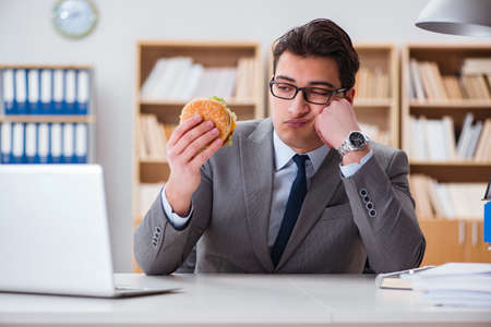 Hungry funny businessman eating junk food sandwichの写真素材