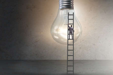 Businessman on ladder with light bulbの写真素材