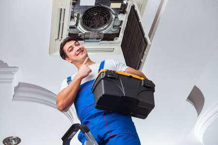 Worker repairing ceiling air conditioning unitの写真素材