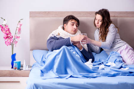 Wife caring for sick husband at home in bedの写真素材