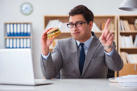 Hungry funny businessman eating junk food sandwichの写真素材