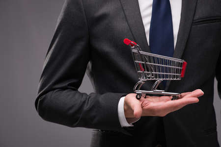 Businessman with shopping cart on gray backgroundの写真素材