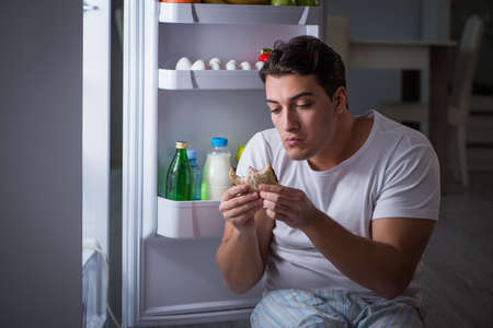 Man at the fridge eating at nightの写真素材