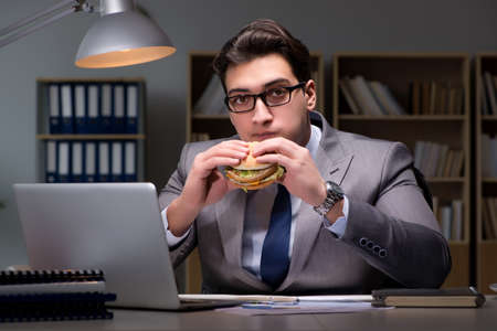 Businessman late at night eating a burgerの写真素材