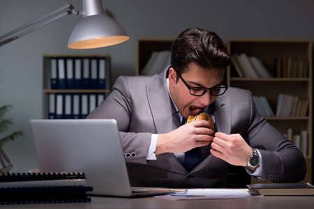 Businessman late at night eating a burgerの写真素材