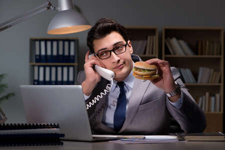 Businessman late at night eating a burgerの写真素材