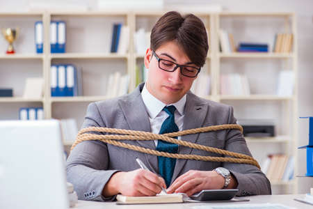 Businessman tied up with rope in officeの写真素材