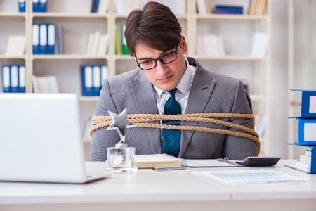 Businessman tied up with rope in officeの写真素材