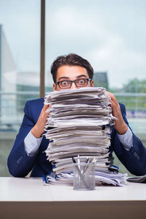 Businessman with pile stack of paper paperwork in the officeの写真素材