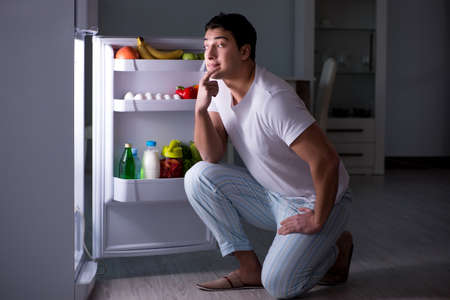 Man at the fridge eating at nightの写真素材