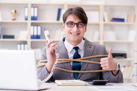 Businessman tied up with rope in officeの写真素材