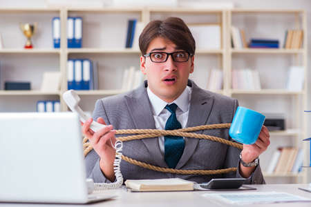Businessman tied up with rope in officeの写真素材