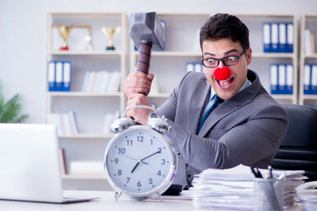 Clown businessman in the office with hammer and an alarm clockの写真素材