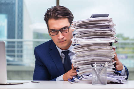 Businessman with pile stack of paper paperwork in the officeの写真素材