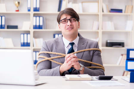 Businessman tied up with rope in officeの写真素材