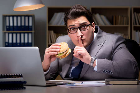 Businessman late at night eating a burgerの写真素材