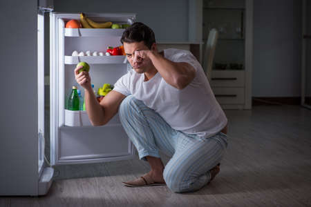 Man at the fridge eating at nightの写真素材