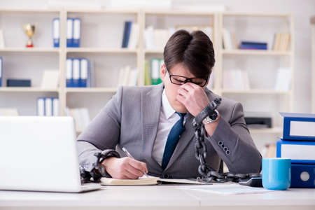 Businessman tied with chains to his workの写真素材