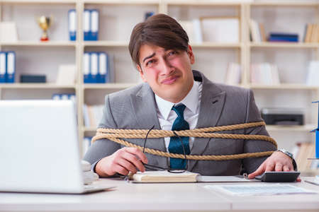 Businessman tied up with rope in officeの写真素材