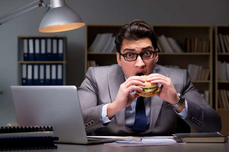 Businessman late at night eating a burgerの写真素材