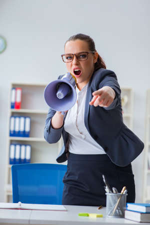 Angry businesswoman yelling with loudspeaker in officeの写真素材
