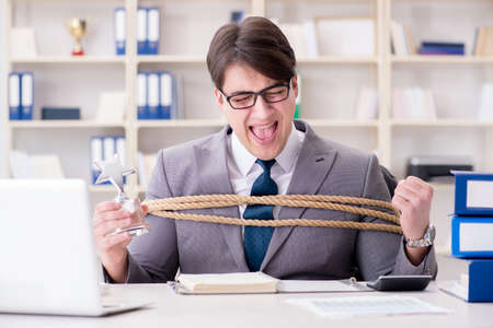 Businessman tied up with rope in officeの写真素材