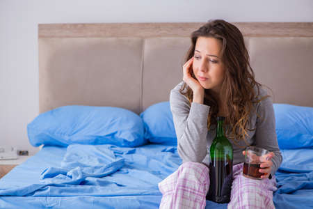 Young woman drinking alcohol depressed at homeの写真素材