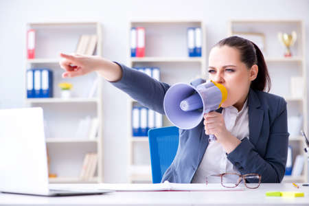 Angry businesswoman yelling with loudspeaker in officeの写真素材