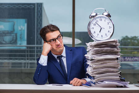 Businessman with pile stack of paper paperwork and an alarm clocの写真素材