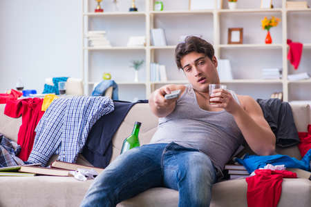 Young man student drunk drinking alcohol in a messy roomの写真素材