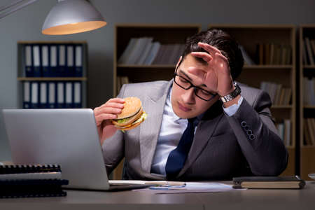 Businessman late at night eating a burgerの写真素材