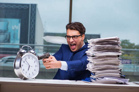 Businessman with pile stack of paper paperwork and an alarm clocの写真素材