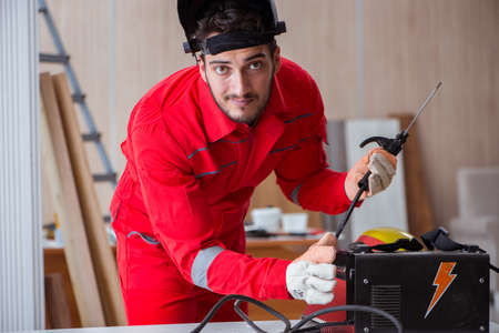 Young repairman with a welding gun electrode and a helmet weldin