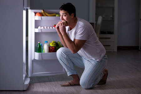 Man at the fridge eating at nightの写真素材
