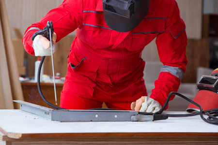 Young repairman with a welding gun electrode and a helmet welding metal
